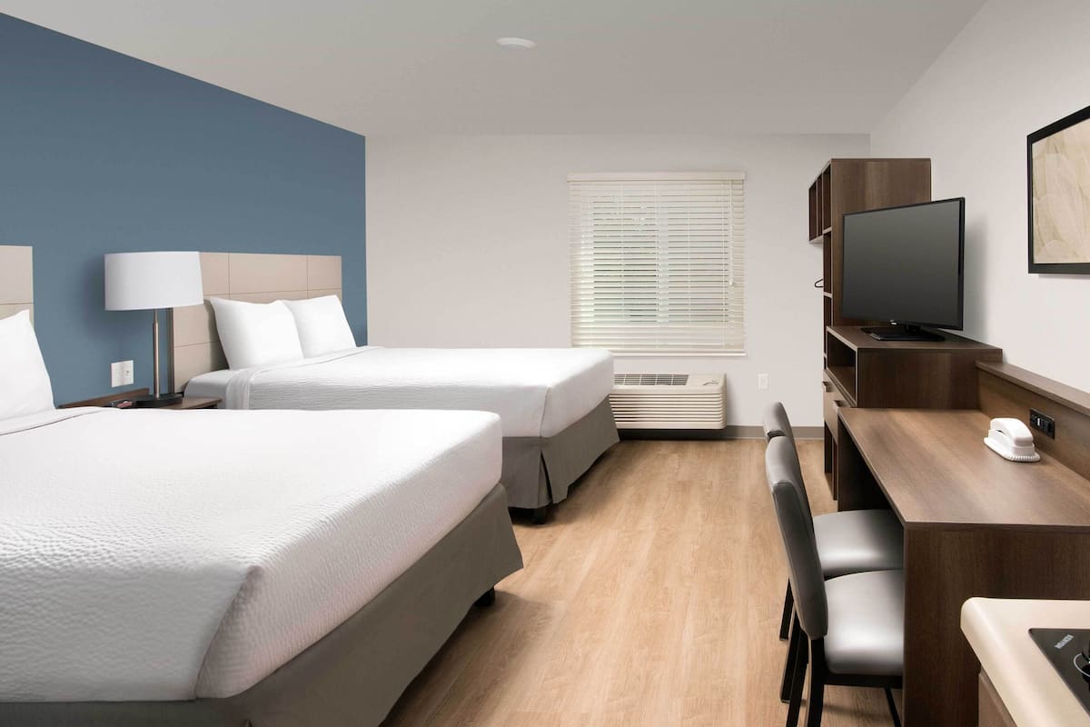 A hotel room with two beds, a desk with a chair, a television, and a window with blinds.