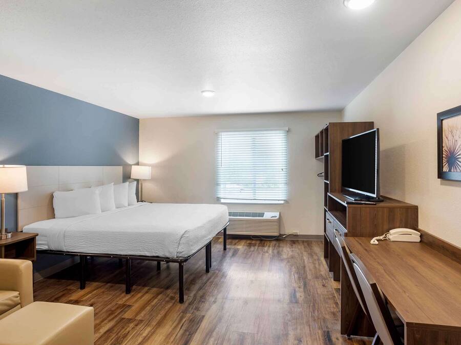 A hotel room with a bed, bedside lamps, a desk, a telephone, a television, and a window with blinds.