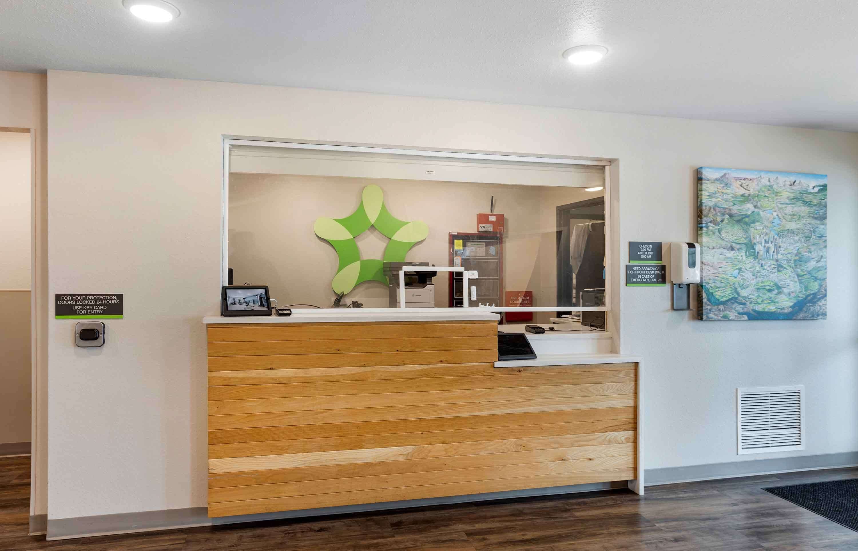 Een houten receptiebalie, een groene decoratieve wanddecoratie, een kaart aan de muur en een bordje dat het gebruik van een sleutelkaart aangeeft.