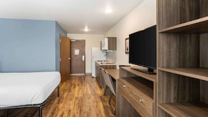 Ein kleines Zimmer mit Bett, Küchenzeile und Fernseher auf einem Holzboden.