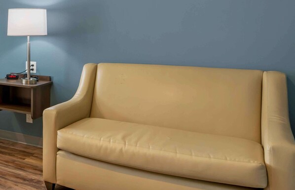 Un sofá color beige frente a una pared azul, una mesita con una lámpara y un enchufe.