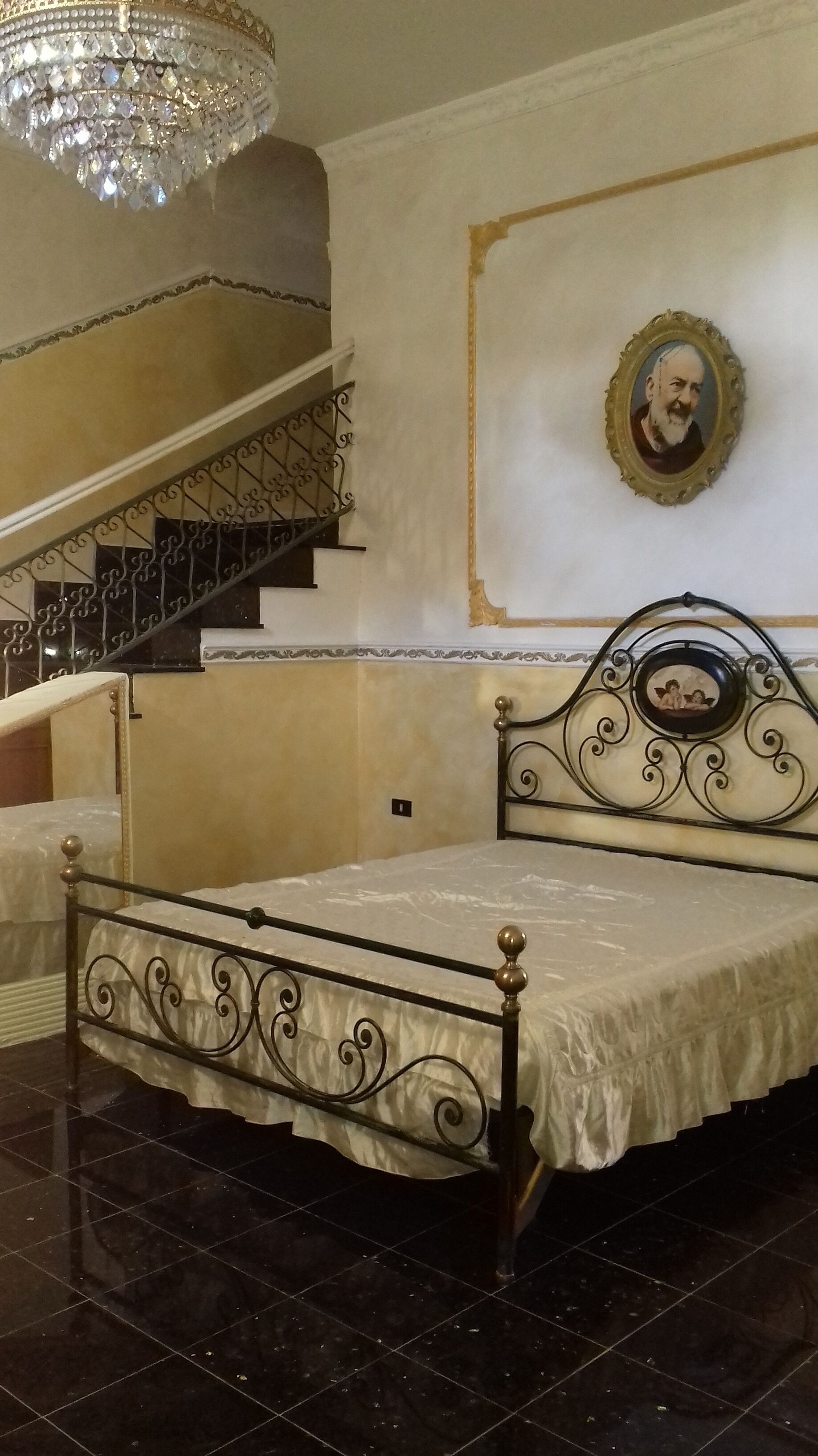Ein Schlafzimmer mit einem Bett, einer Kristallleuchter, einer Treppe und einem gerahmten Bild an der Wand.