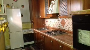 Eine Küche mit Holzschränken, einem Gasherd, einer Spüle, einem Kühlschrank und einem Herd mit schwarzem Backofen.