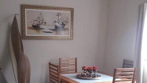 A dining area with a wooden table and chairs, a framed artwork above, and a surfboard leaning against the wall.