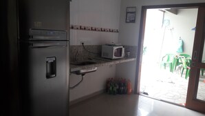 A kitchen with a refrigerator, microwave, sink, and a small countertop. There are plastic chairs outside the door.