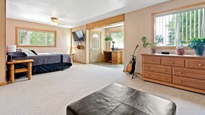 A bedroom with a bed, bedside table, lamp, and a large window with blinds.