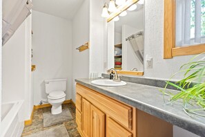 Un bagno con un water bianco, mobili in legno, un piano di lavoro in granito e uno specchio illuminato.