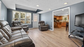 A modern living room with a leather sofa, a recliner, and a flat-screen TV on a stand.