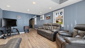 A modern living room with a leather sofa, a recliner, and a flat-screen TV on a stand.