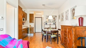 Une cuisine moderne avec des meubles en bois, un coin repas avec une table et des chaises, et un salon avec un canapé et un plaid.
