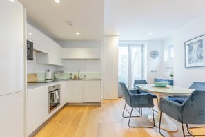 A modern kitchen with white cabinets, a built-in oven, and a dining area with a table and chairs.