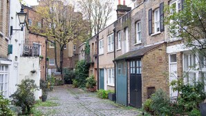 A narrow cobblestone street flanked by traditional brick buildings with white doors and shutters.