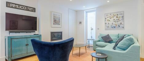 Un salon moderne avec un fauteuil bleu, un canapé turquoise et un téléviseur à écran plat posé sur un meuble.