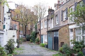 A narrow cobblestone street flanked by traditional brick buildings with white doors and shutters.