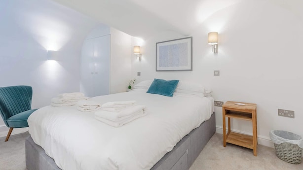 Ein Schlafzimmer mit einem Bett, einem Sessel, einem Nachttisch und einer Wandleuchte.