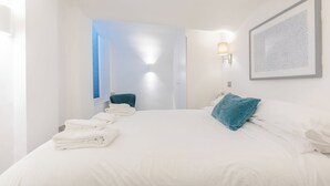 A hotel room with a bed, a window, a wall-mounted light, and a framed picture.