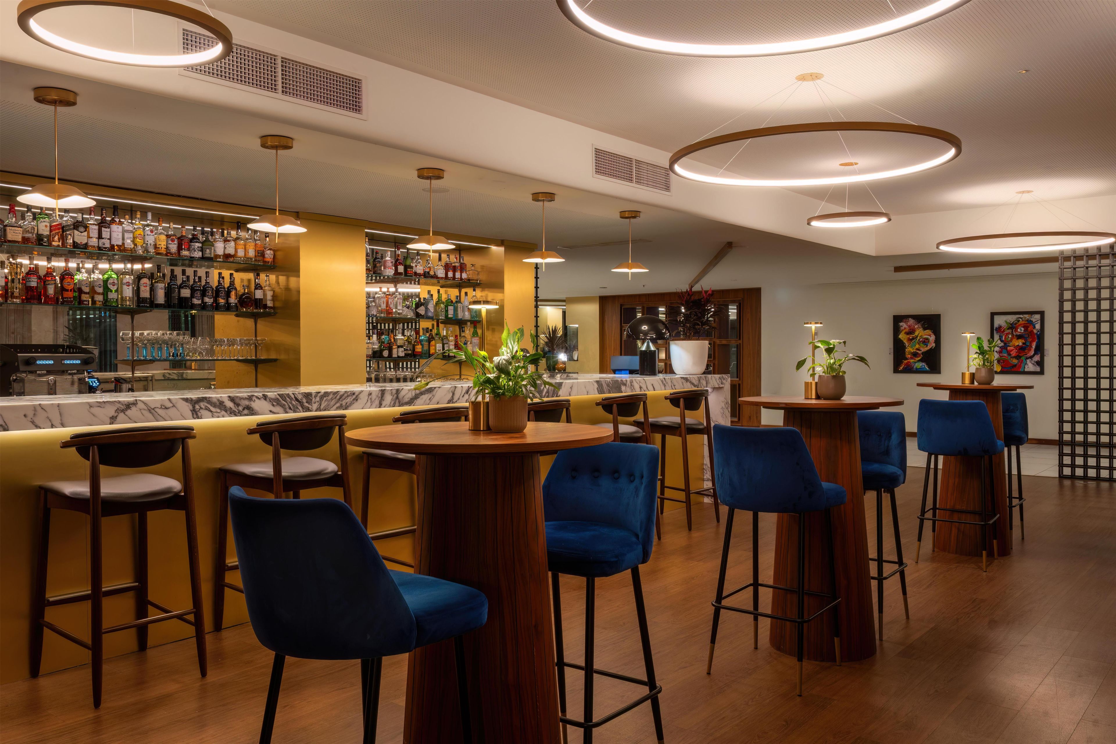 A bar area with multiple seating options, a well-stocked liquor shelf, and a modern ceiling design.