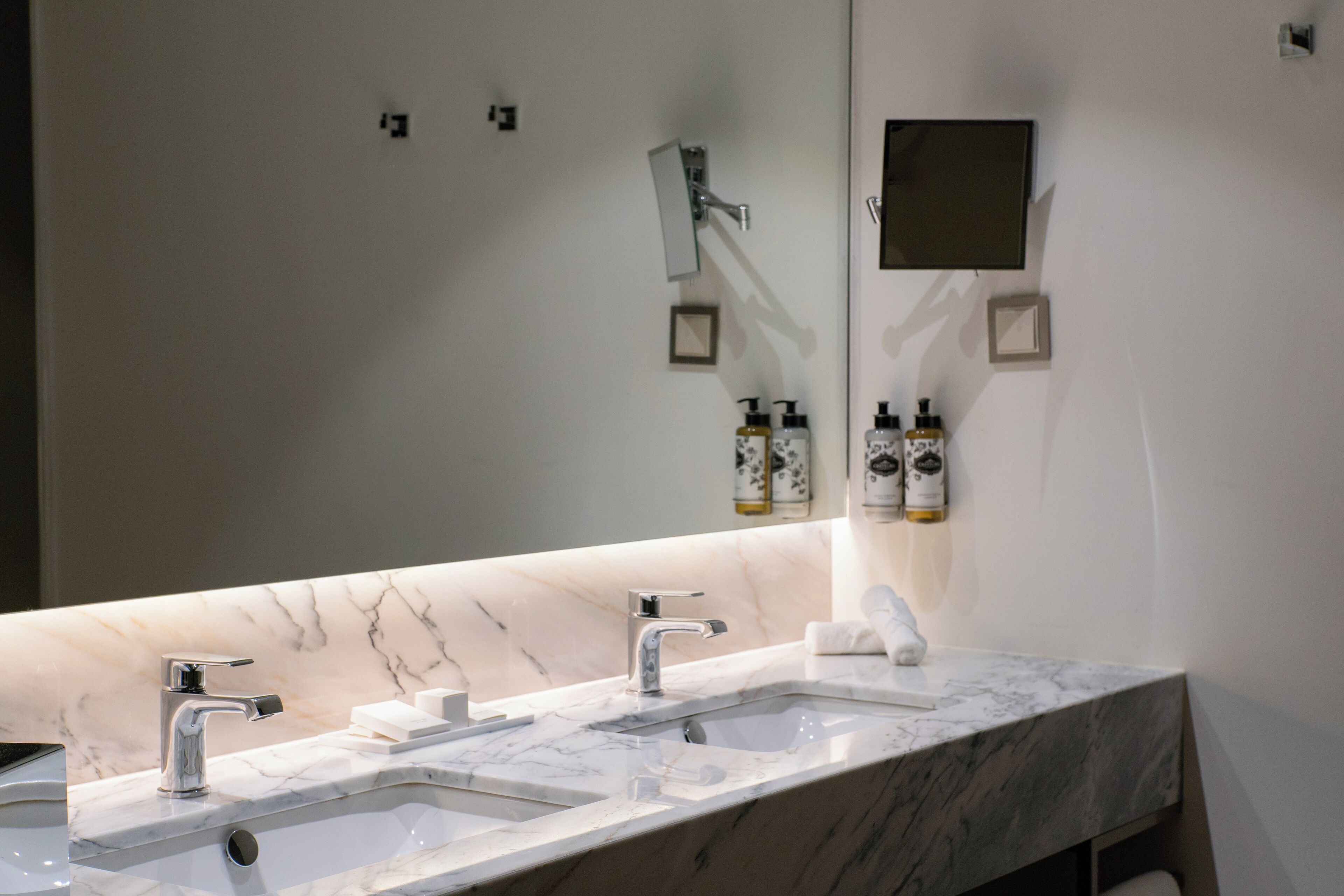 A modern bathroom with two sinks, a large mirror, and toiletries on the wall.