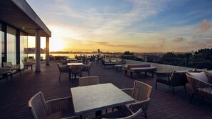 Una terraza en la azotea con mobiliario exterior, vistas del horizonte urbano y un atardecer.