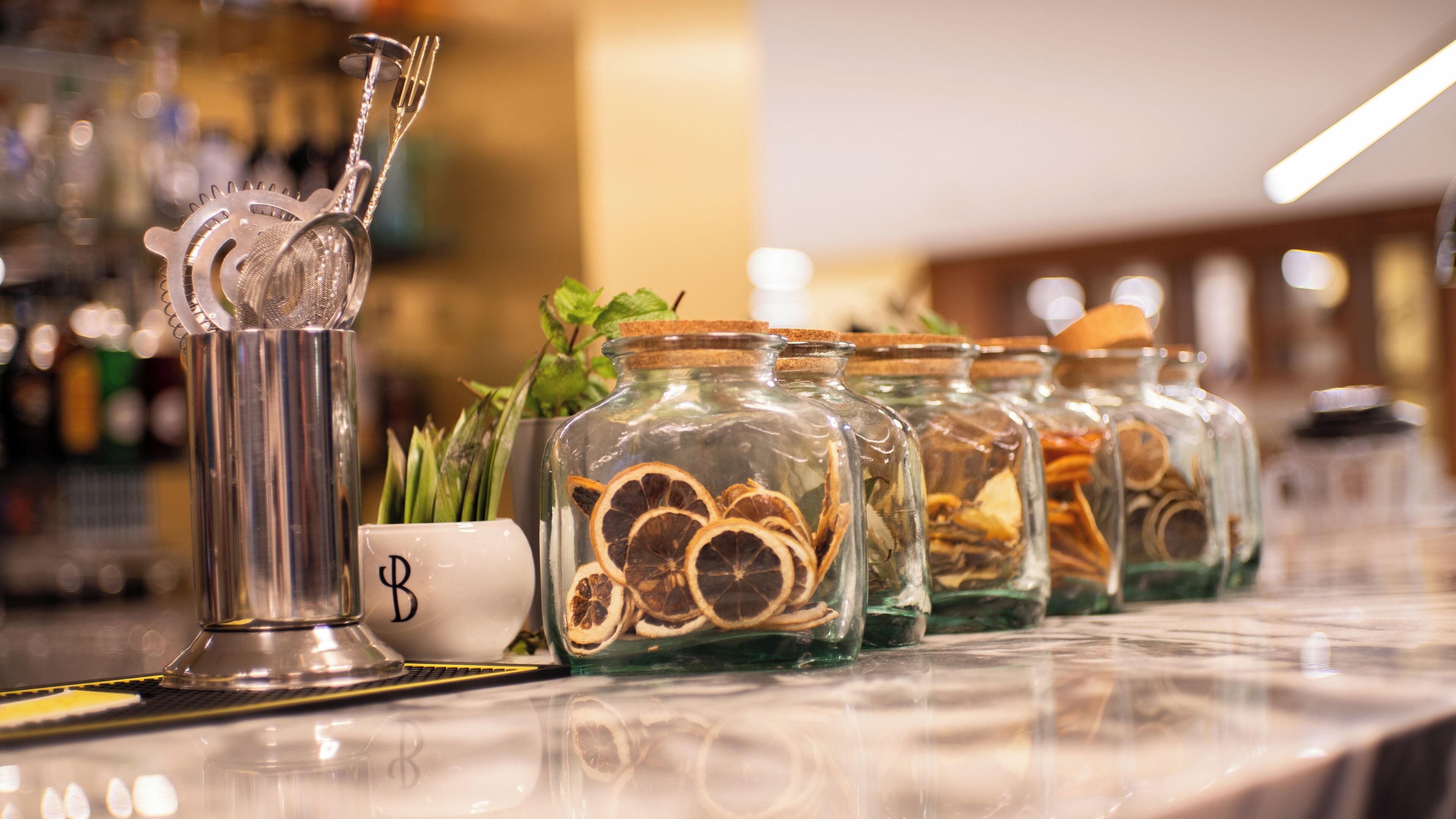 A bar area with a metal strainer, a white mug with a letter, and glass jars containing dried fruits.