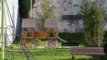 Explore the adjacent playground with a climbing structure, slide, and playhouse, set amidst lush greenery and a nearby bench for seating.