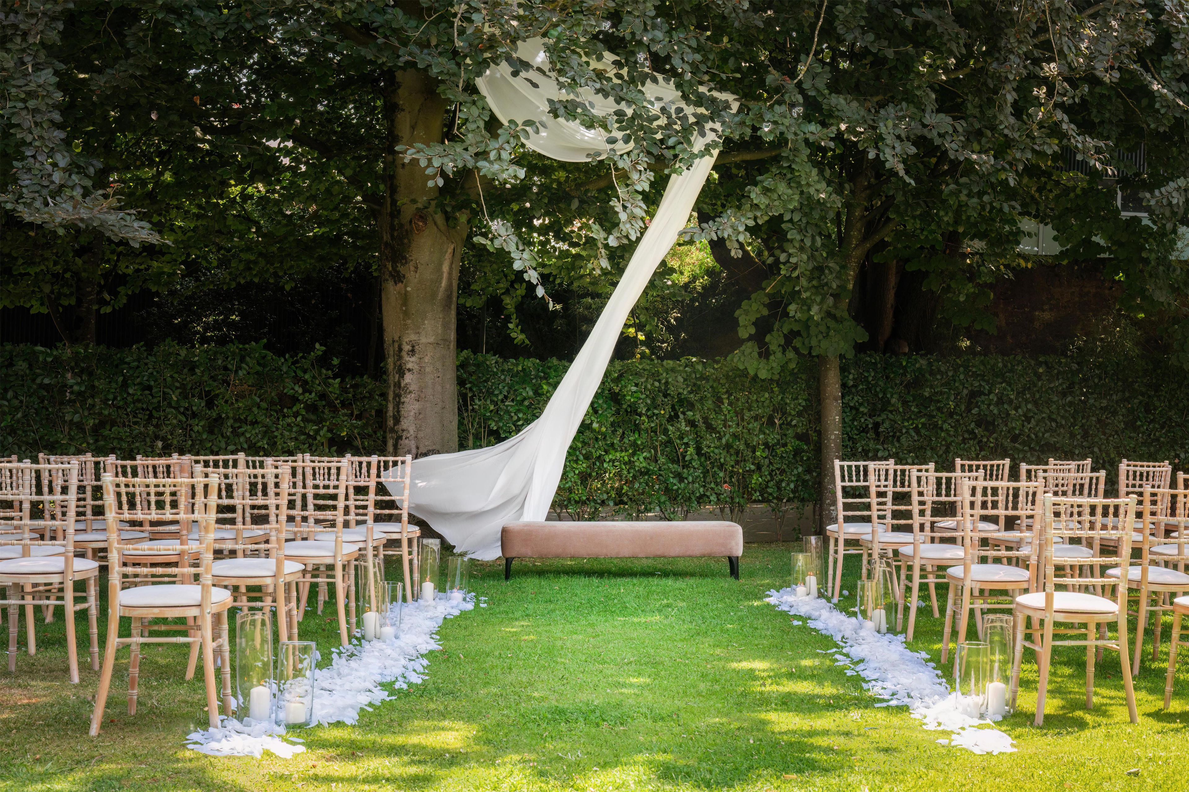 Decoración para una boda al aire libre con un pasillo blanco, sillas de madera y un banco.