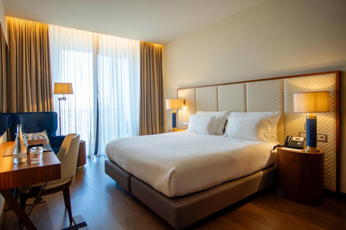A hotel room with a bed, bedside tables, a desk, and a chair.