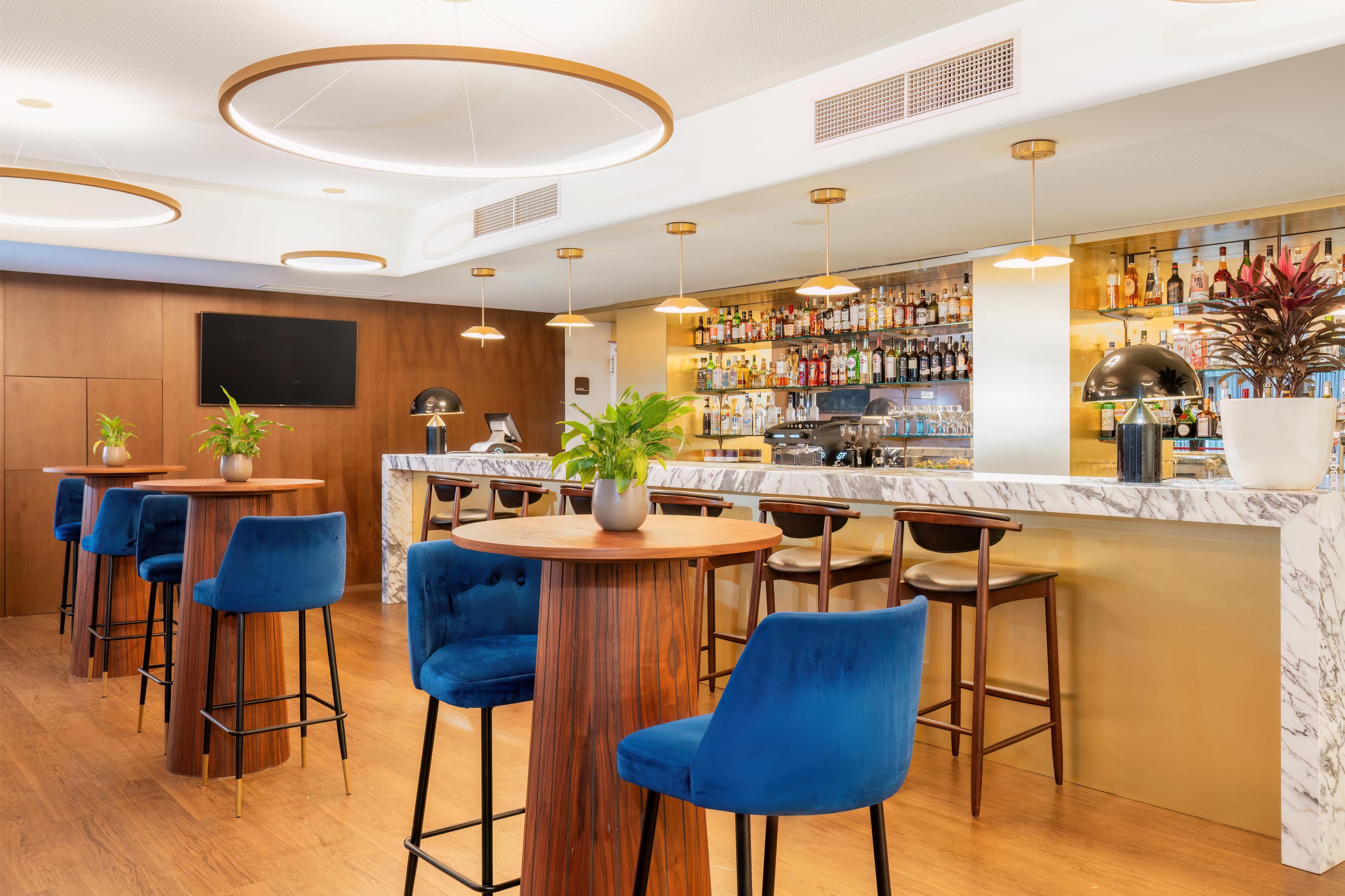 A bar area with wooden bar stools, a marble counter, and a variety of bottles on shelves.