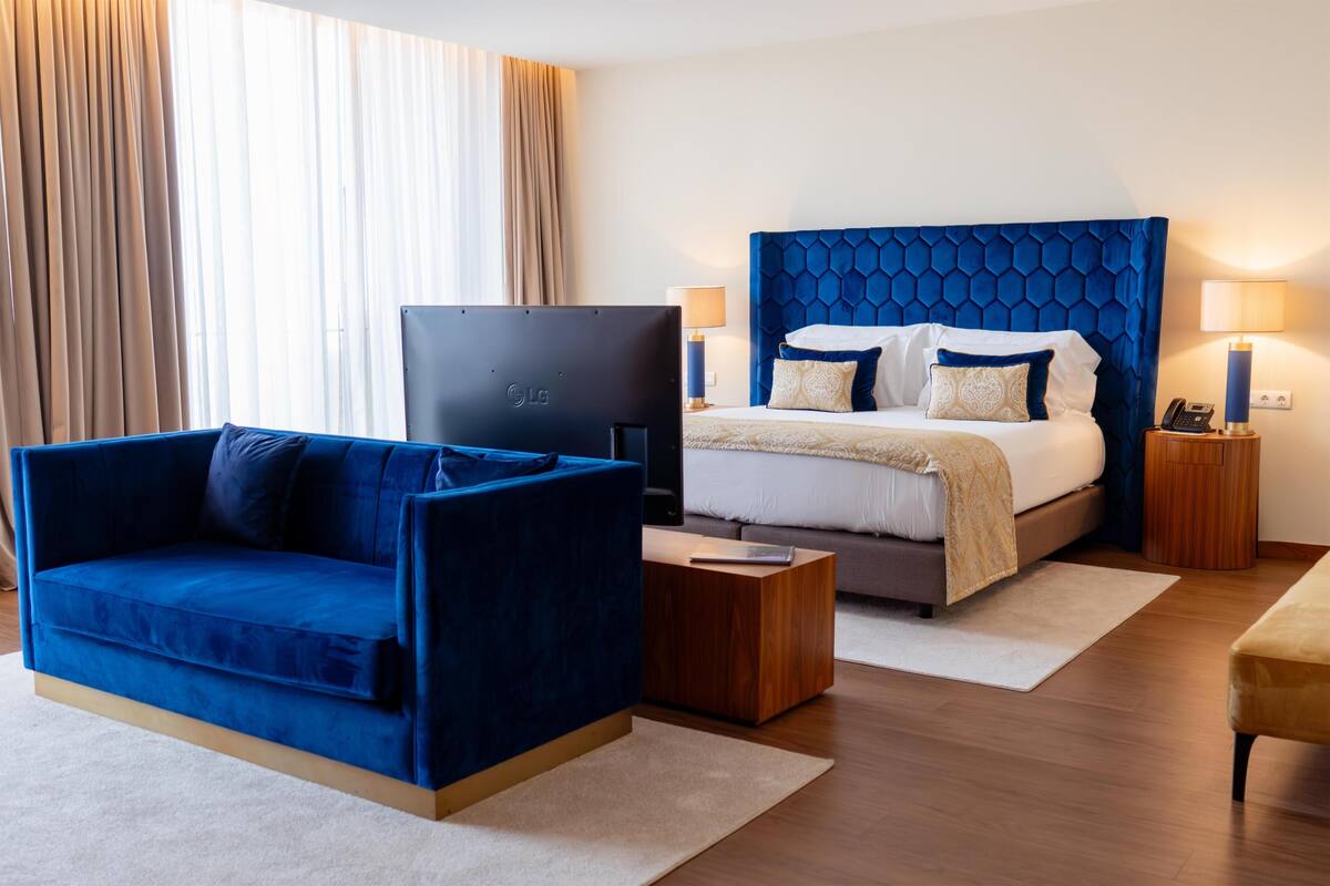 A hotel room with a bed, a blue sofa, a TV, and a bedside table.