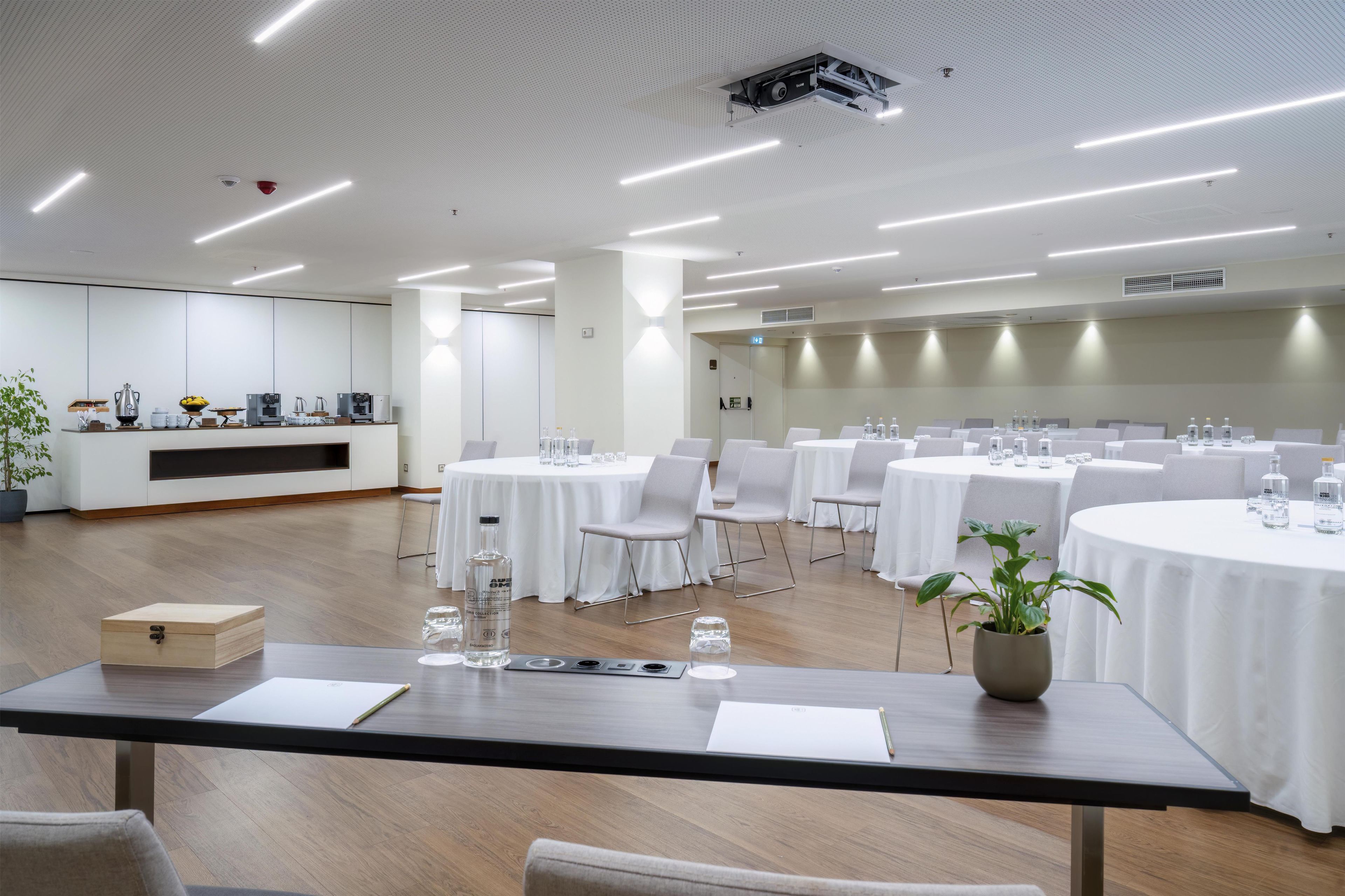 Une salle de conférence équipée de tables rondes, de chaises et d’un coin café.