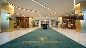 A hotel lobby with a green carpet, reception desk, seating area, and a central table.