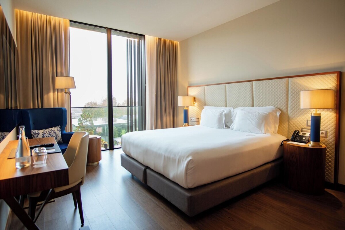 Una habitación de hotel con una cama grande, un escritorio con silla, un teléfono y una lámpara.