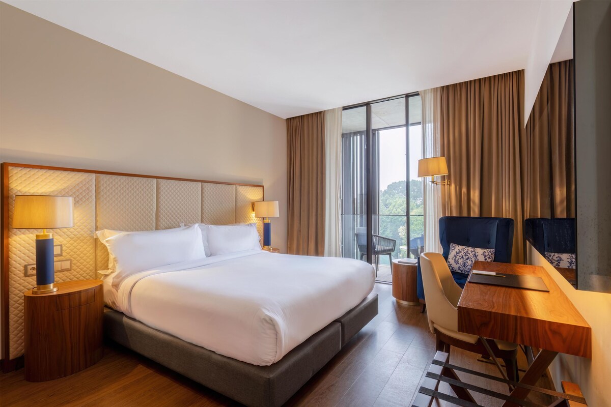 Une chambre d’hôtel avec un grand lit, des lampes de chevet, un bureau avec une chaise et une vue par la fenêtre.
