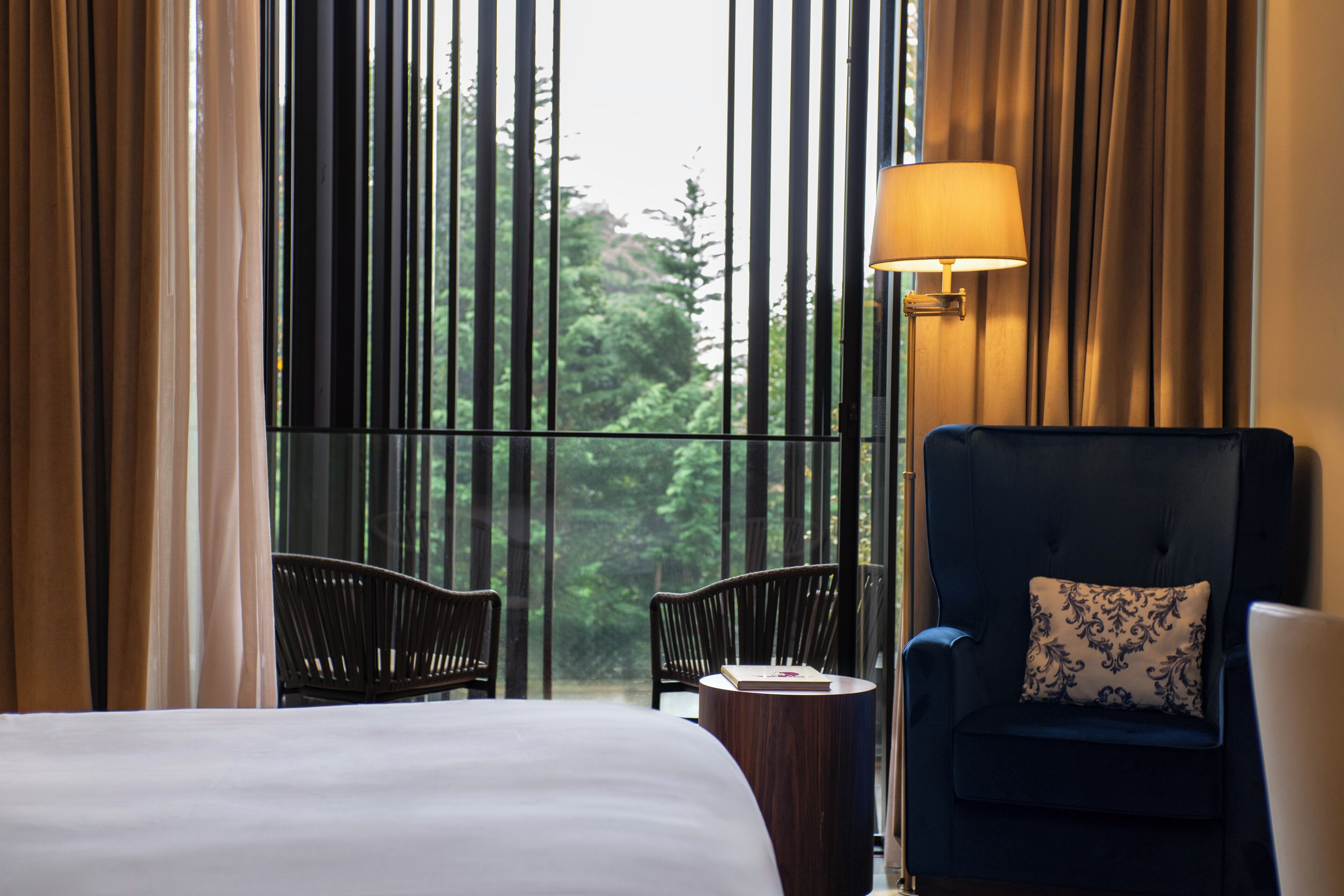 Una habitación de hotel con una cama grande, dos sillones, una mesita y una lámpara.