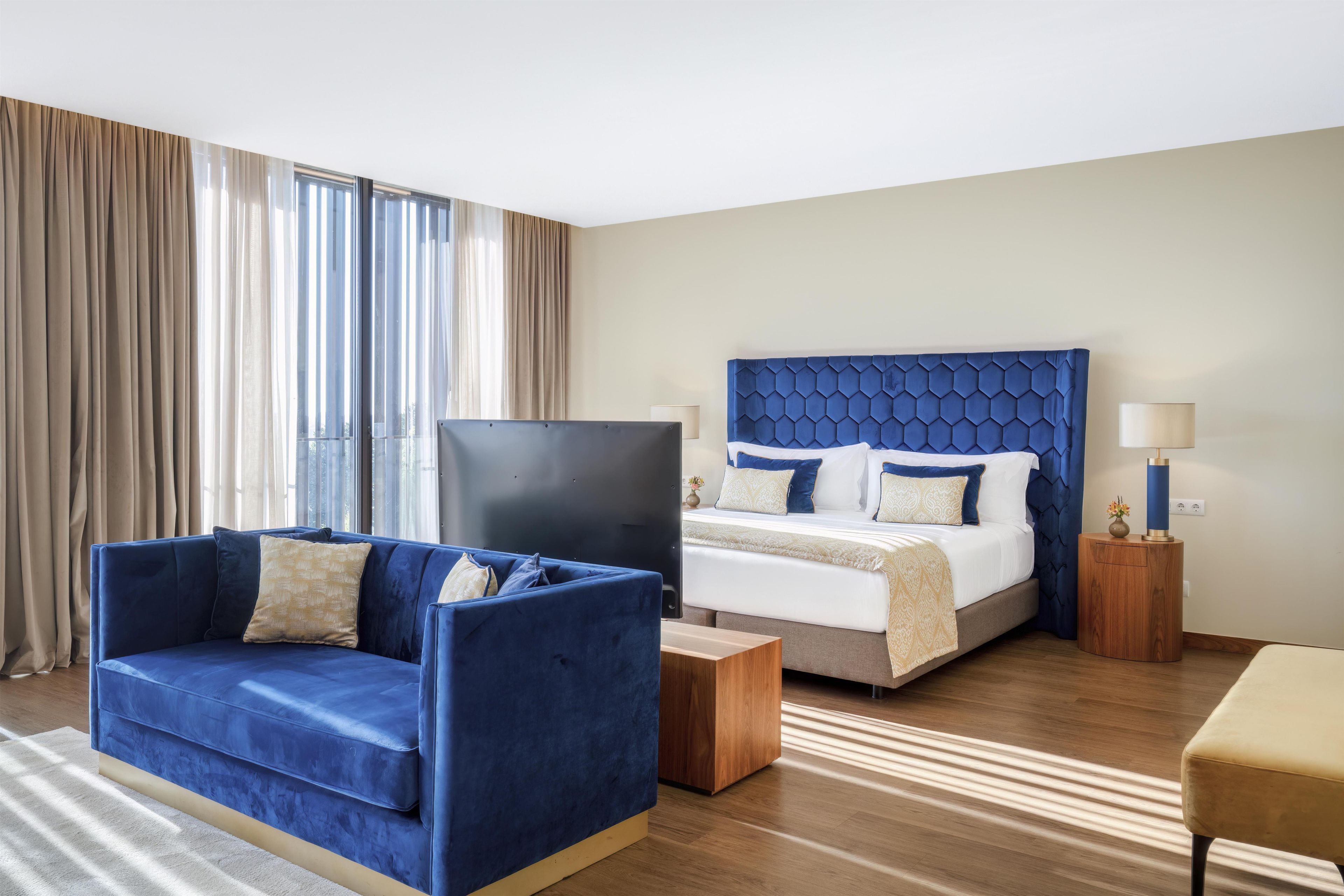 A hotel room with a bed, a sofa, a TV, and a bedside table.