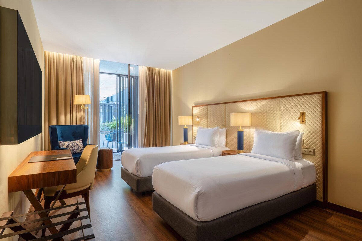 Une chambre d’hôtel avec deux lits, un bureau, une chaise et une vue sur l’extérieur.