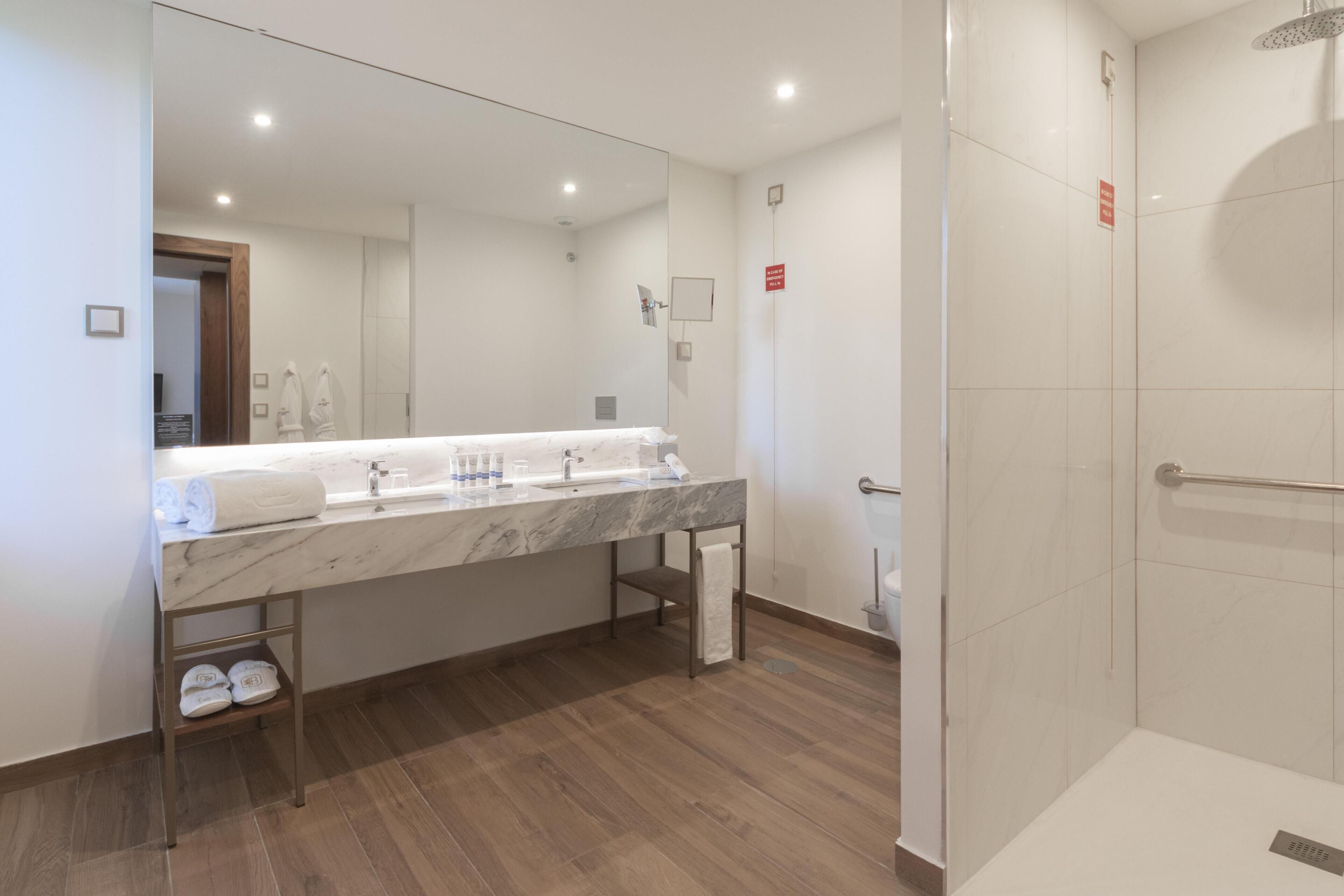 A modern bathroom with a marble vanity, a glass shower enclosure, and a wooden floor.