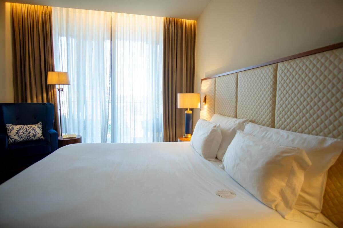 A hotel room with a large bed, a chair, a lamp, and curtains.