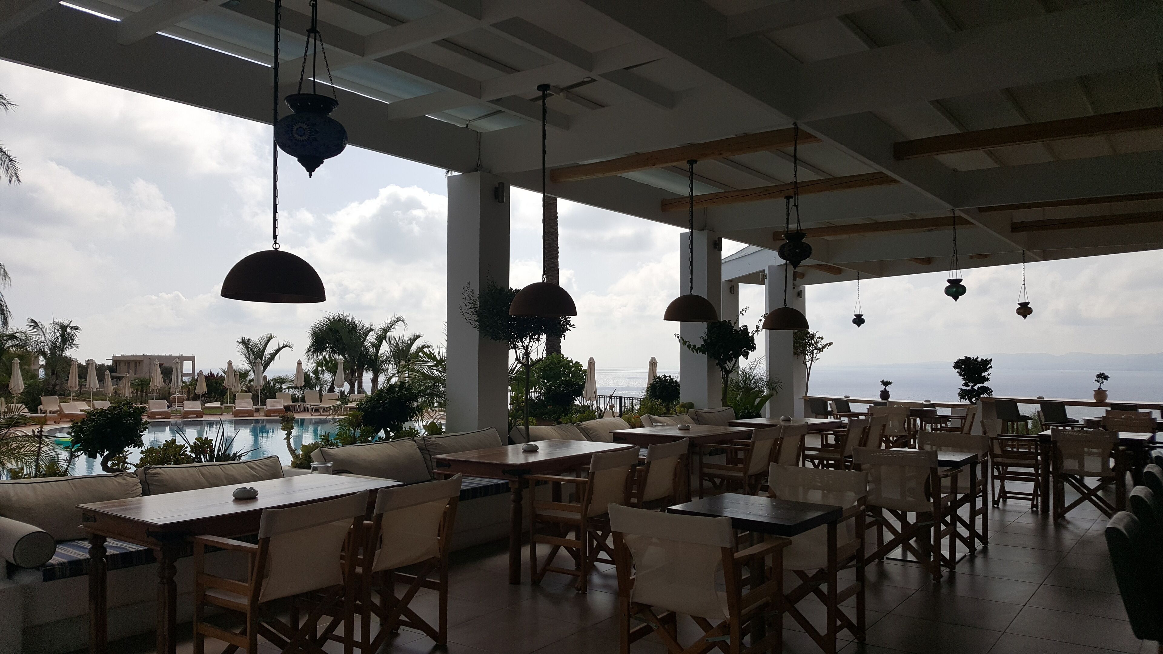 Un área de comedor al aire libre con mesas y sillas, con vista a una piscina y al mar.