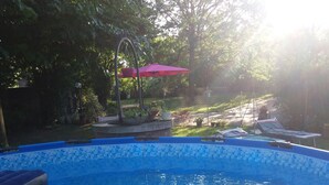 A clear blue swimming pool with a tiled edge, surrounded by greenery and a red umbrella. - B&B Un mondo a Colori (Ferrara)