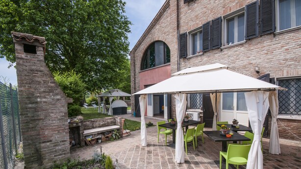 A patio with a table and chairs, a brick wall, and a building with windows and shutters. - B&B Un mondo a Colori (Ferrara)