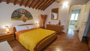 A bedroom with a wooden bed, a nightstand with a lamp, a dresser, and a painting on the wall. - B&B Un mondo a Colori (Ferrara)
