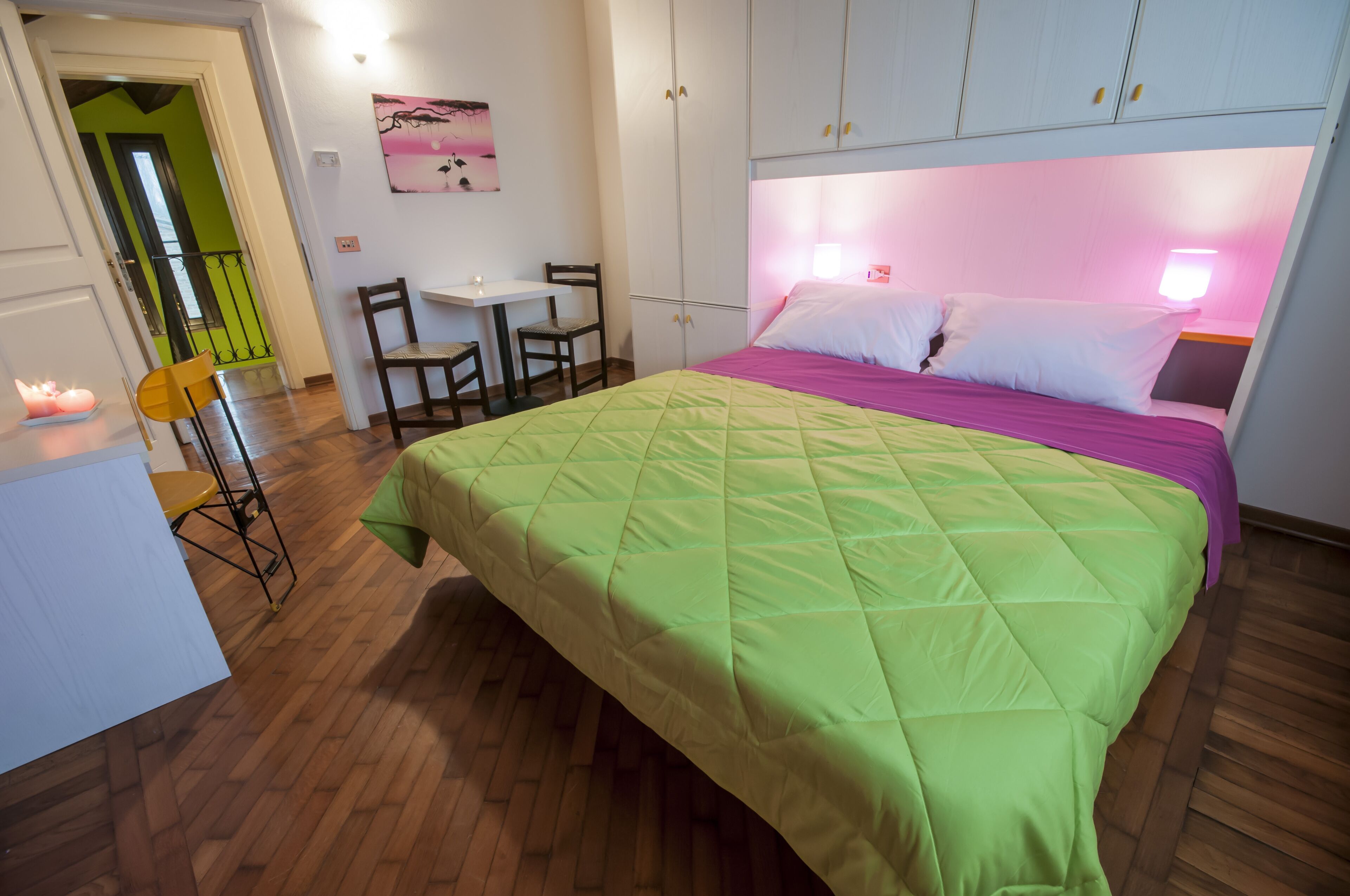 A bedroom with a bed, a desk, chairs, and a painting on the wall.