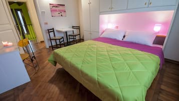 A bedroom with a bed, a desk, chairs, and a painting on the wall.