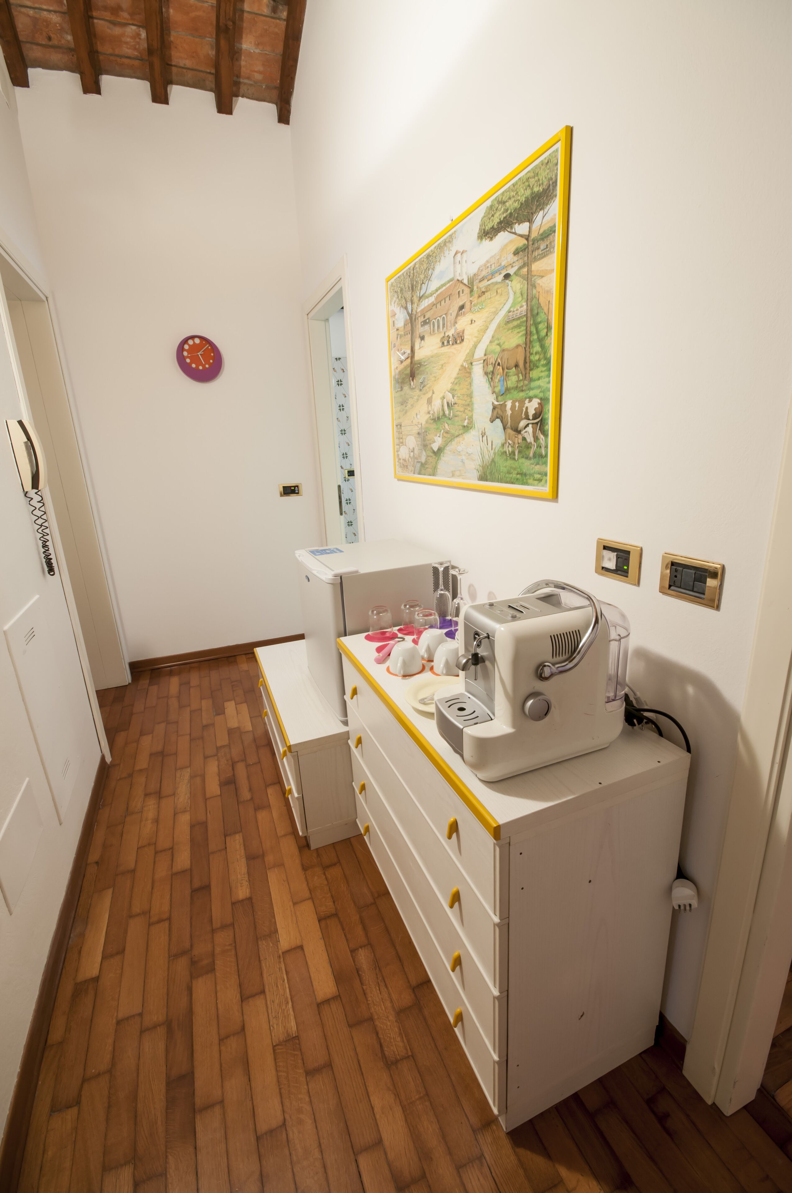 A small kitchen with a wooden floor, a white refrigerator, a sink, and a painting on the wall.
