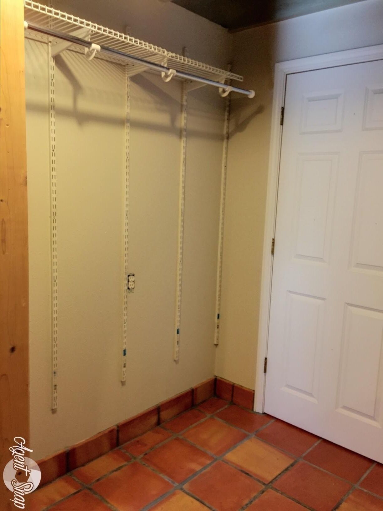 A corner of a room with a white door, a tiled floor, and a metal shelving unit against the wall.