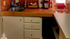 A kitchen with a tiled backsplash, a sink, a countertop with various items, and a set of drawers. - Studio Apartment in Historic Neighborhood (Amarillo)