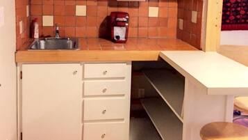 Una cocina compacta con un fregadero, una cafetera y una estantería con platos decorativos.