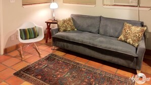 A living room with a grey sofa, patterned cushions, a small white chair, a floor lamp, and a patterned rug. - Studio Apartment in Historic Neighborhood (Amarillo)