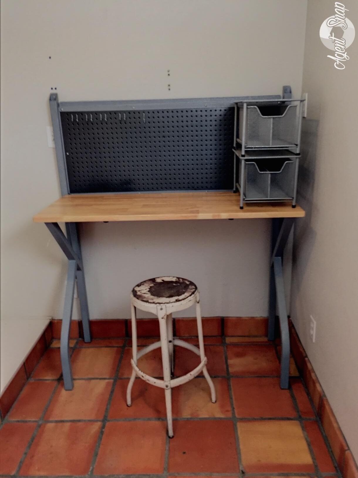 Un espacio de trabajo en esquina con un escritorio de madera, panel posterior de malla metálica y un taburete blanco.